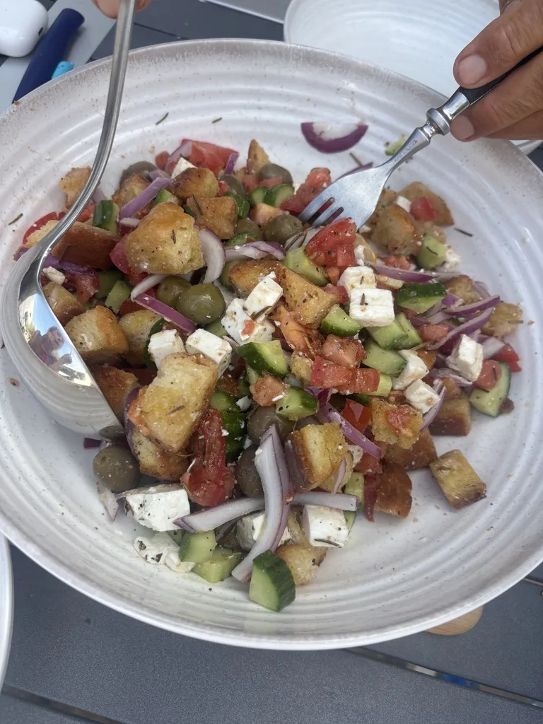 Bunter Brotsalat mit gerösteten Brotwürfeln, Tomaten, Gurken, roten Zwiebeln, Oliven und Feta in einer weißen Schüssel