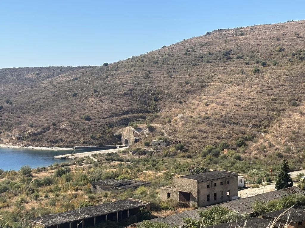 Bucht von Porto Palermo mit dem alten Betontunnel aus der Hoxha-Zeit im Hügel, davor verlassene Militärgebäude