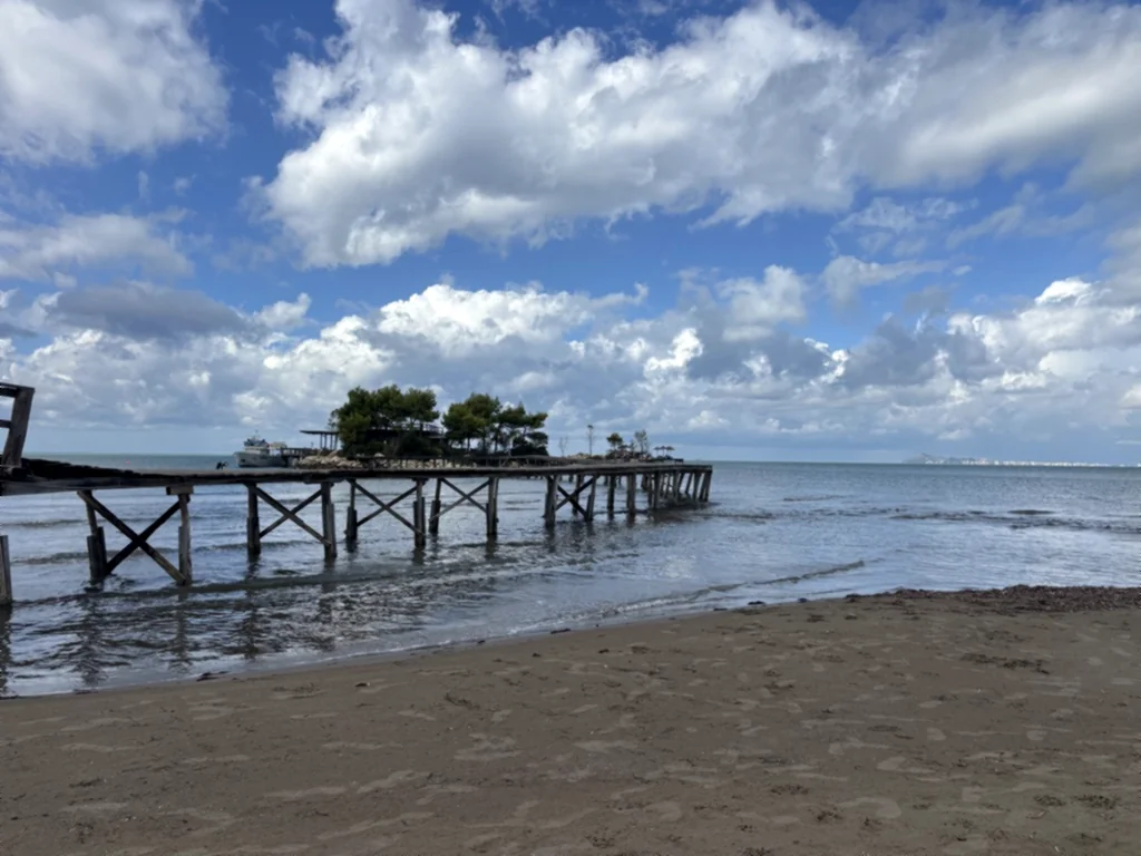 Langer Holzsteg führt vom Sandstrand übers Meer zu einer kleinen Insel mit Bäumen