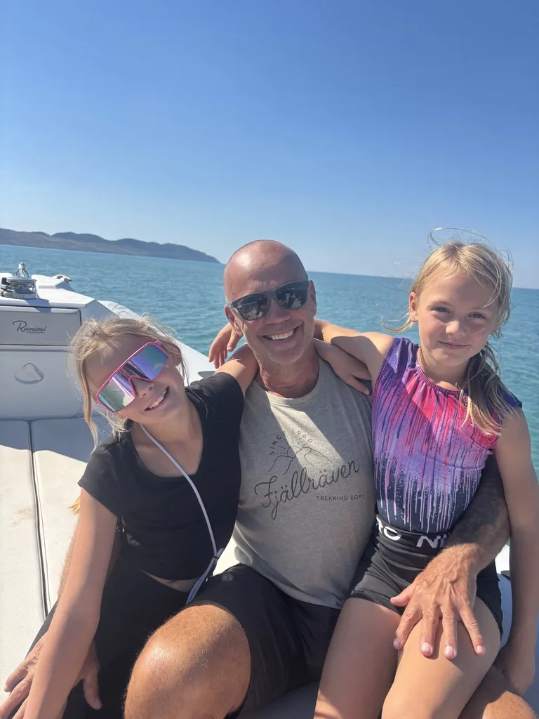 Heiner sitzt lachend zwischen Franziska und Anna im Boot, dahinter Meer und Küste