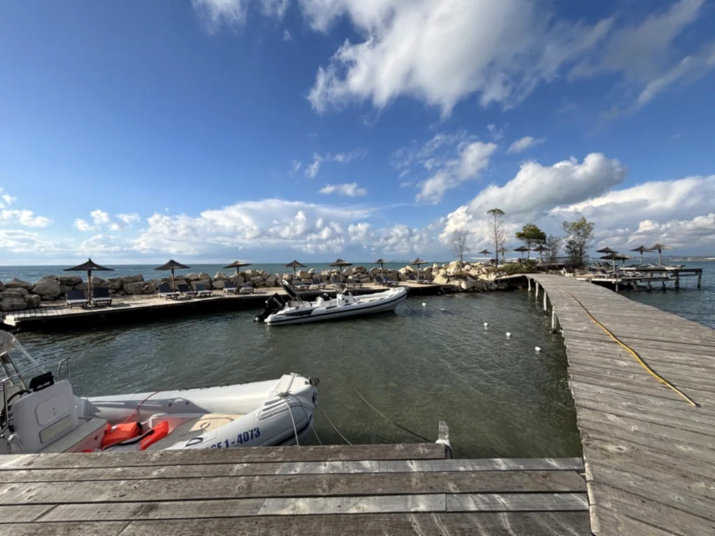 Schlauchboote am Holzsteg, dahinter Liegen und Sonnenschirme aus Stroh auf der kleinen Insel