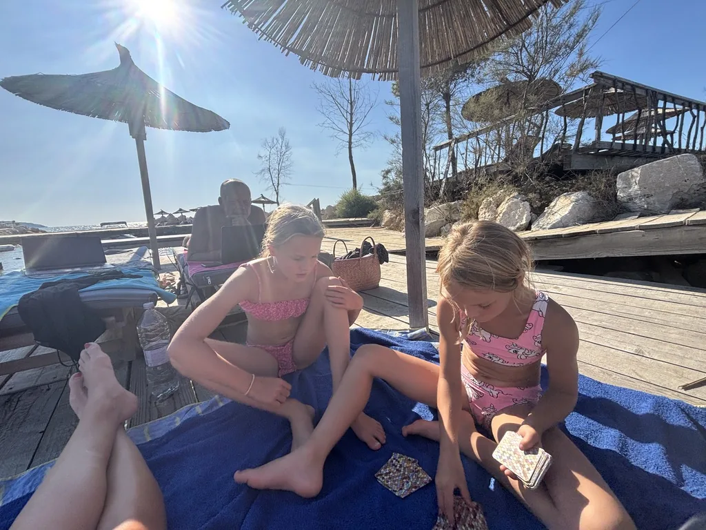 Franziska und Anna spielen Karten auf einem blauen Handtuch unter Schirmen aus Schilf