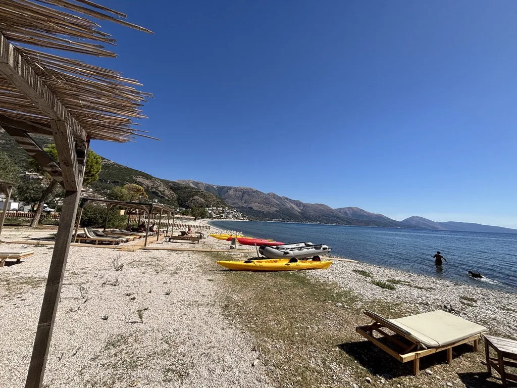 Kiesstrand mit gelben und roten Kajaks und einem Schlauchboot, dahinter Berge und das ruhige Meer