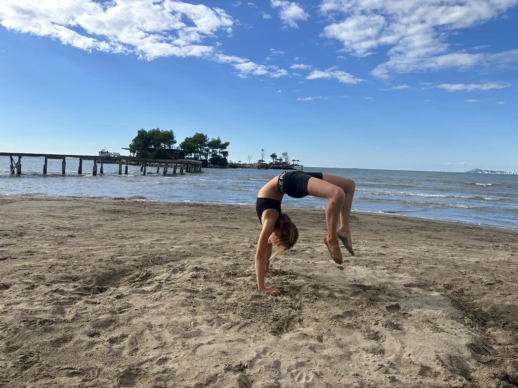 Ein Kind turnt eine Brücke im Sand vor dem Meer