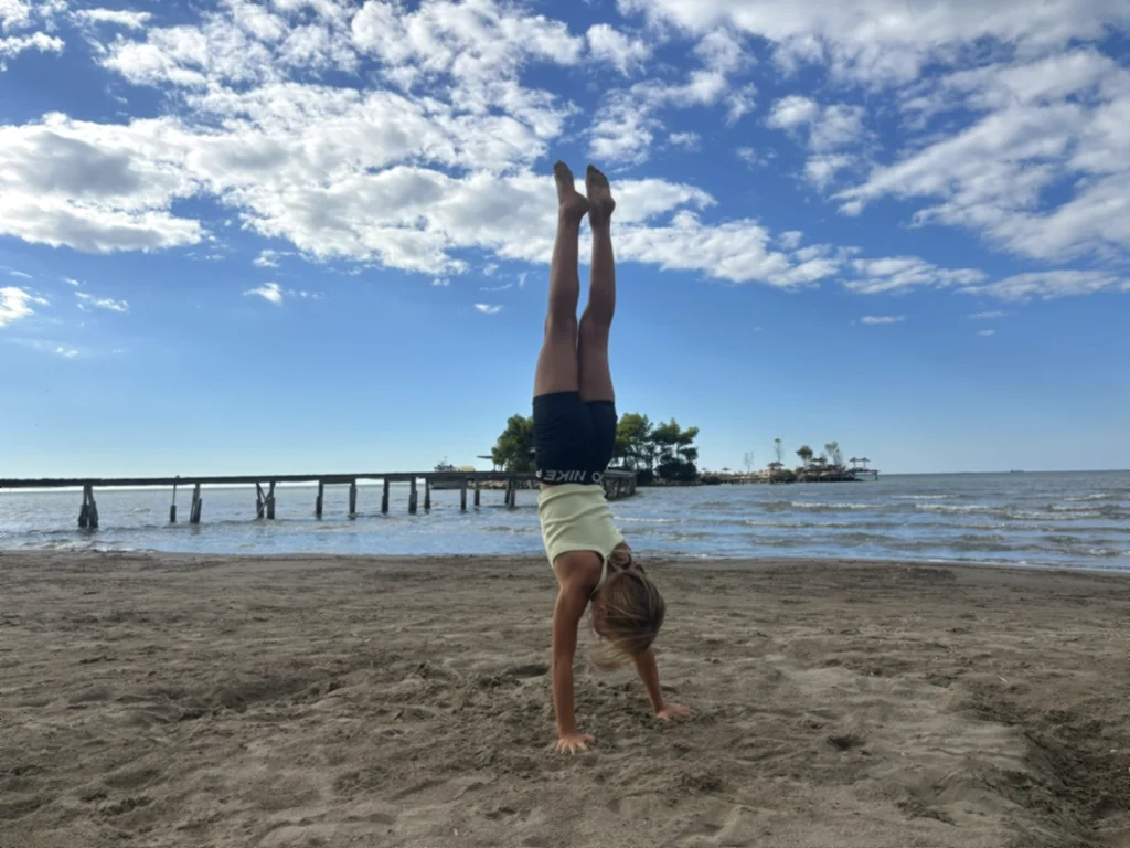 Ein Kind steht kerzengerade im Handstand vor dem Meer und dem Holzsteg