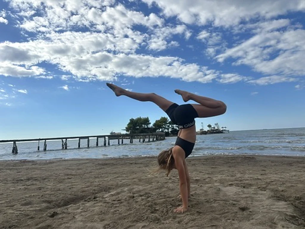 Ein Kind macht einen Handstand mit gespreizten Beinen am Sandstrand