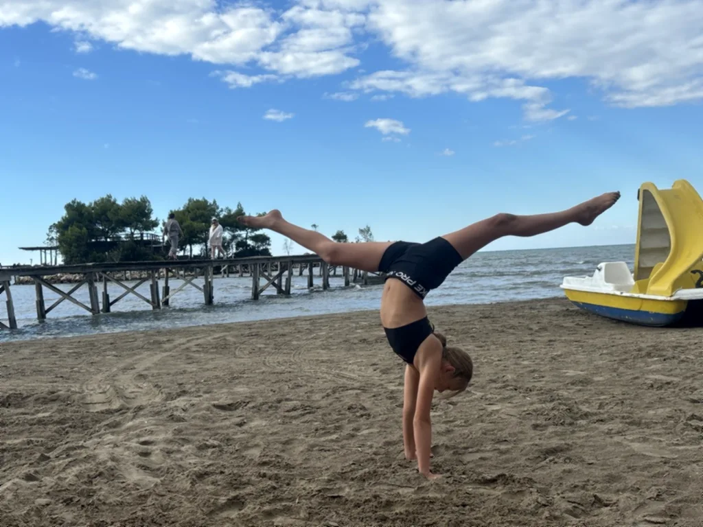 Ein Kind macht einen Handstand mit gegrätschten Beinen neben einem gelben Tretboot