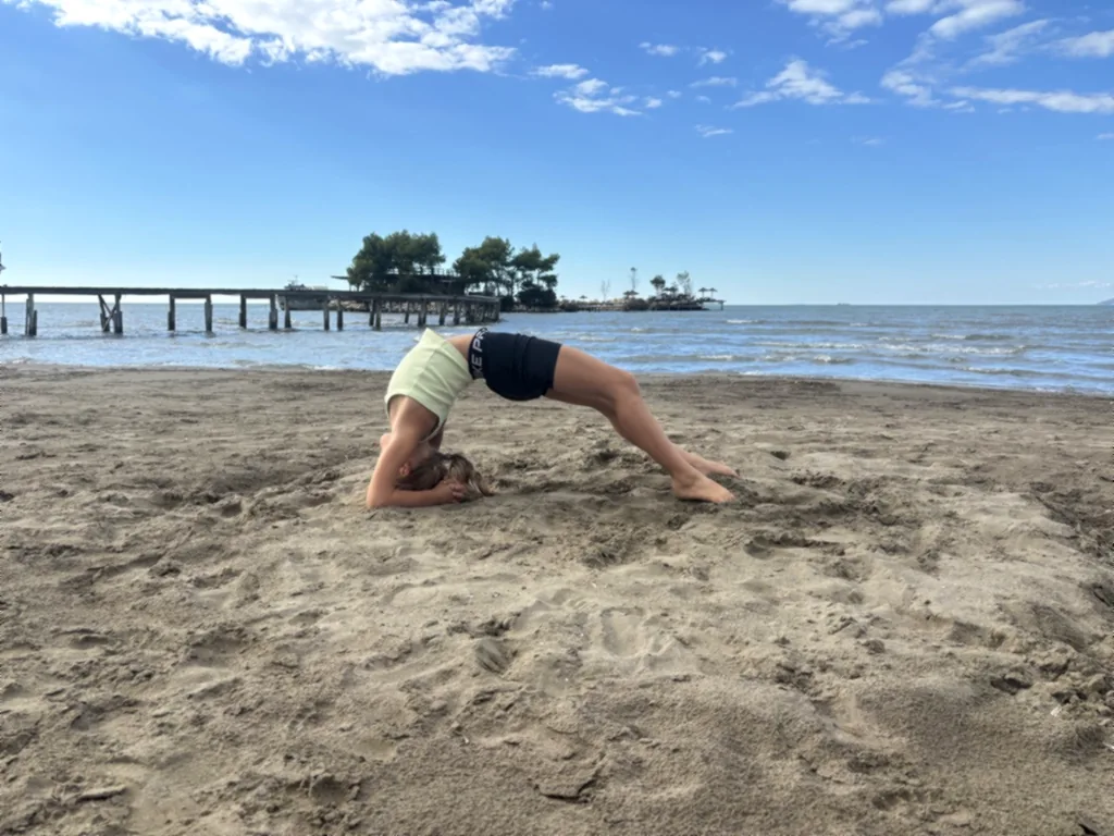 Ein Kind macht eine Brückenvariante mit dem Kopf im Sand