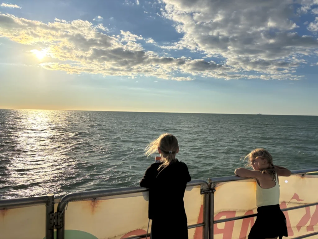 Zwei Kinder lehnen an der Reling und schauen aufs glitzernde Meer