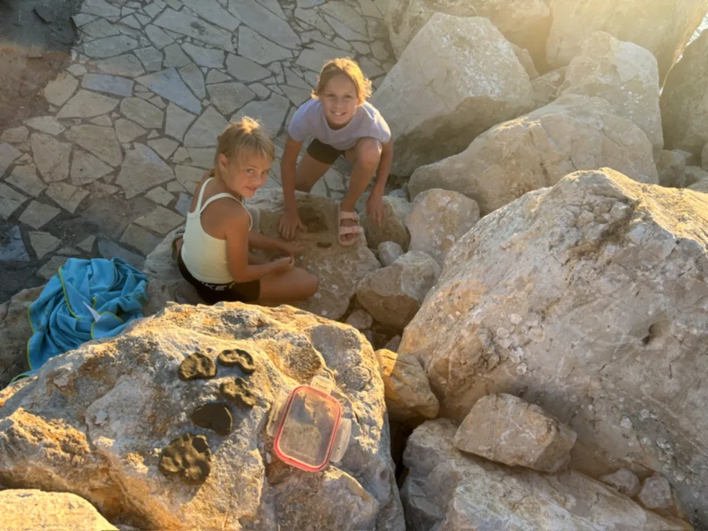 Zwei Kinder formen im Abendlicht Ton auf großen Felsen, daneben eine Box und ein Handtuch