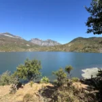 Weiter Blick über den Koman-Stausee auf schroffe Kalkberge unter blauem Himmel
