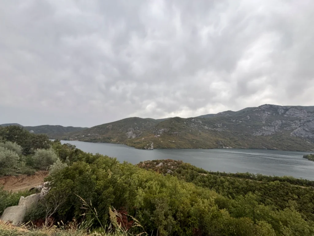 Blick von der Serpentinenstraße auf den Koman-Stausee an einem wolkenverhangenen Morgen