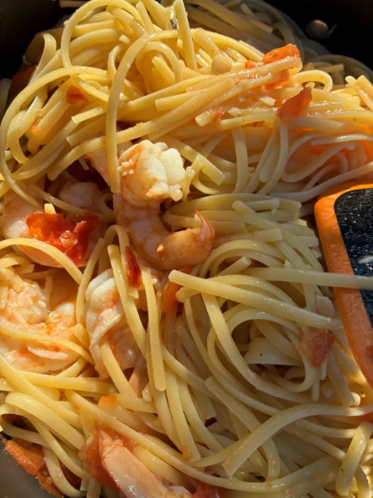 Nahaufnahme von Linguine mit gegarten Scampi, Tomatenstücken und Knoblauch in der Pfanne