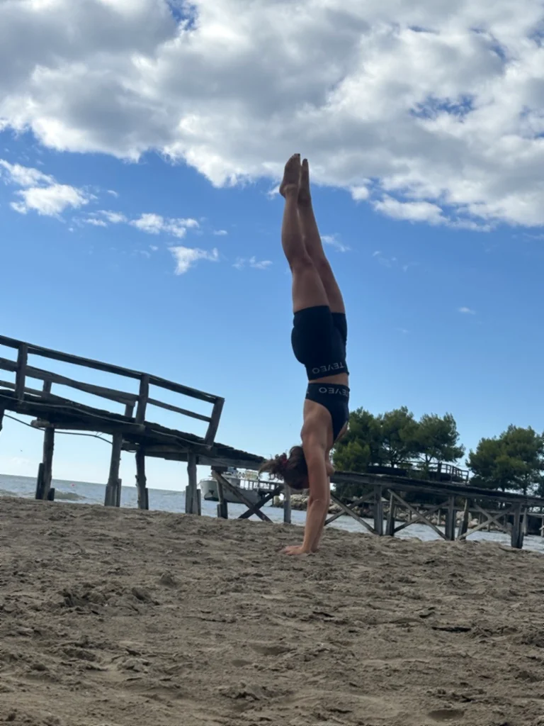 Lisa macht einen geraden Handstand im Sand vor dem Holzsteg