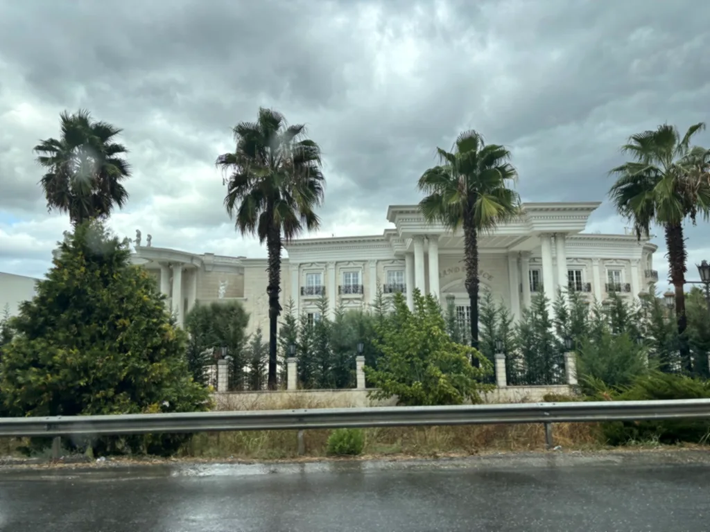 Weißes Gebäude mit Säulen und Palmen, fotografiert aus dem Auto bei Regen