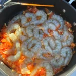 Rohe Scampi in einer Pfanne mit Tomaten, Knoblauch und Öl auf dem Campingkocher