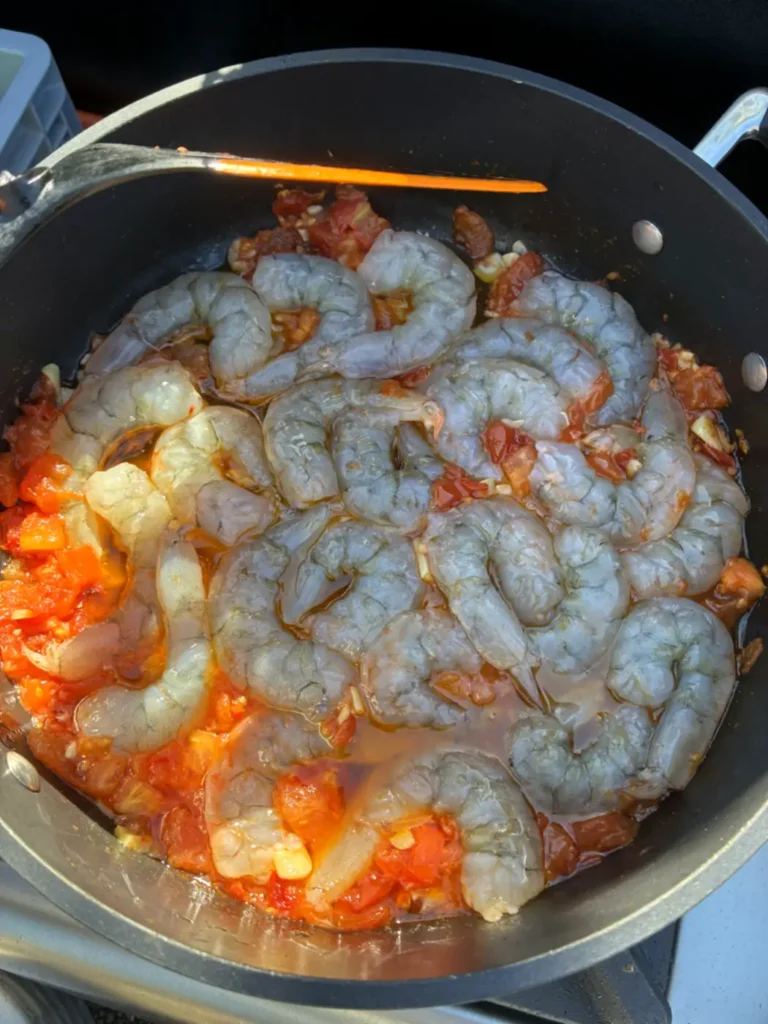 Rohe Scampi in einer Pfanne mit Tomaten, Knoblauch und Öl auf dem Campingkocher