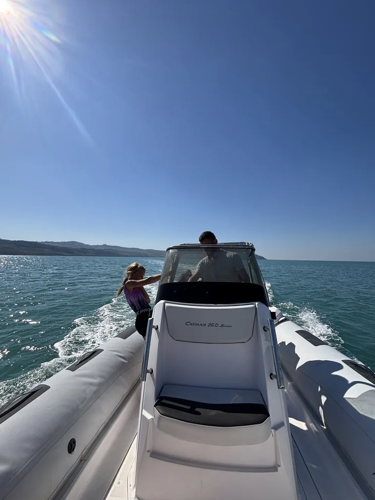 Blick über das Schlauchboot zum Steuerstand, ein Mädchen steht neben dem Fahrer, das Meer glänzt in der Sonne