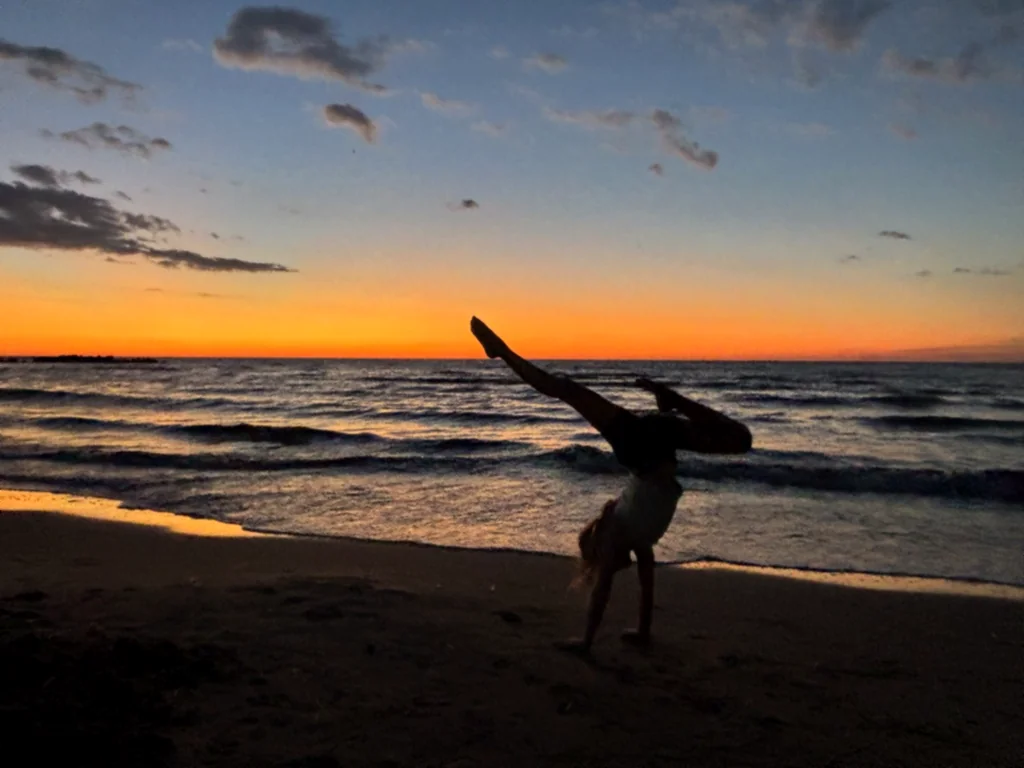 Silhouette eines Kindes im Handstand mit einem gestreckten Bein vor dem Sonnenuntergang
