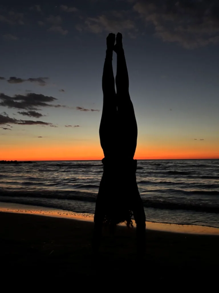 Silhouette eines Kindes im Handstand nah am Wasser in der blauen Stunde