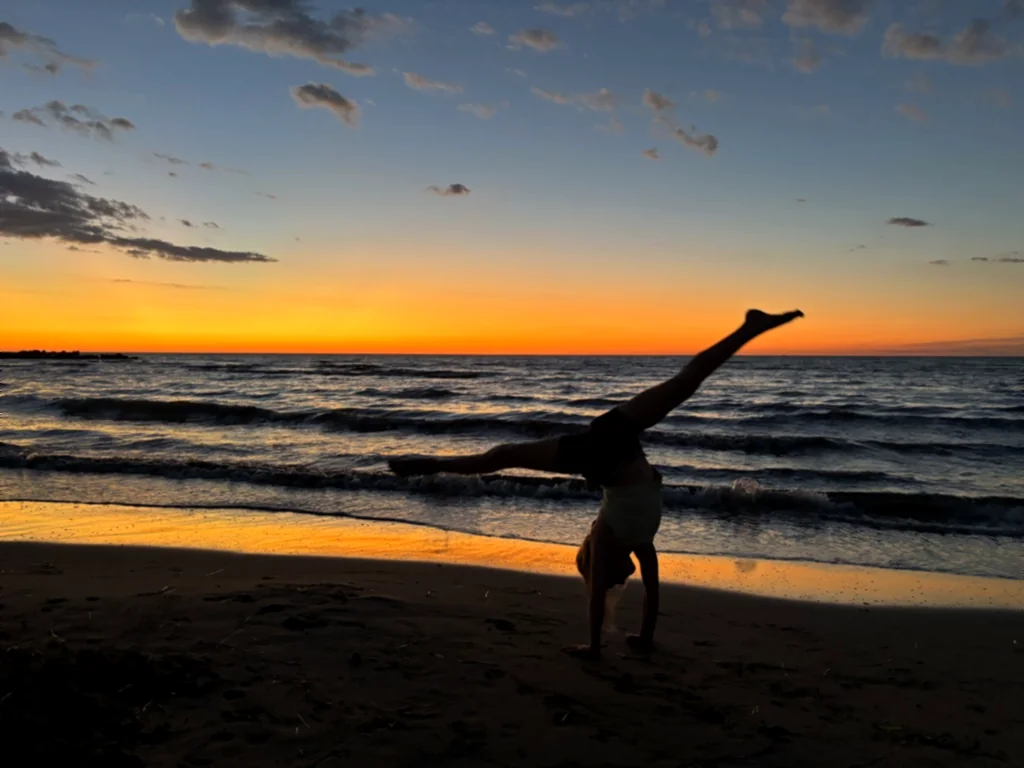 Silhouette eines Kindes beim Radschlagen am Strand vor orangem Horizont