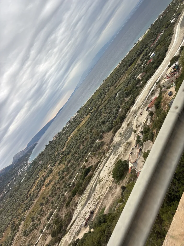 Weiter Blick über ein Tal mit Olivenhainen und Bergketten unter einer grauen Wolkendecke