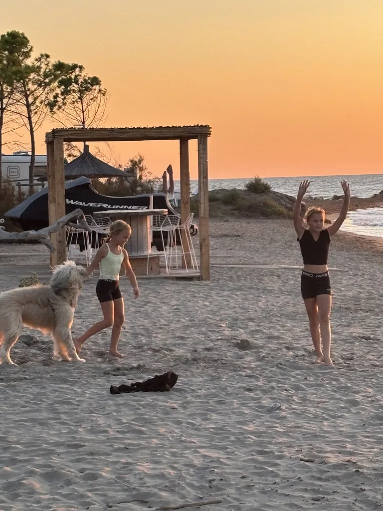 Die Mädchen turnen am Sandstrand im orangen Abendlicht, daneben ein zotteliger Hund